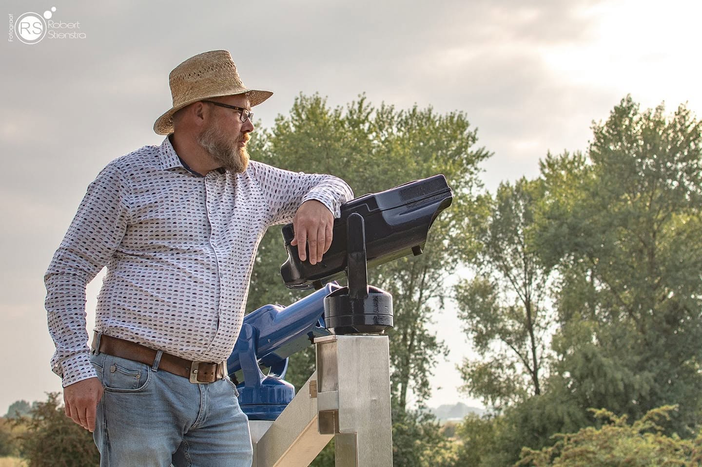 Iwan met strohoed, leunend op een panoramakijker, kijkt uit over het landschap.